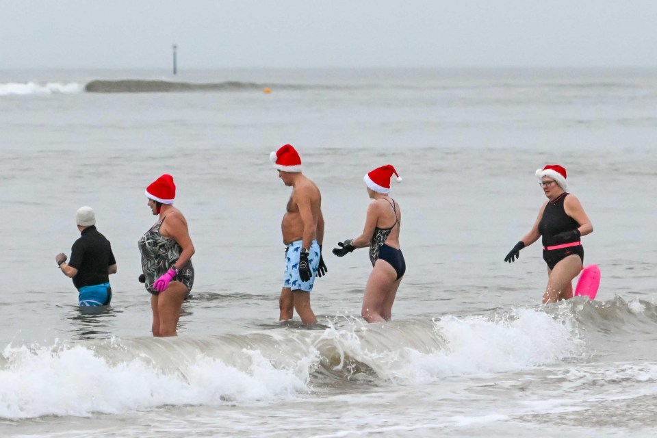 Christmas Day swimmers in Santa hats enter the sea.