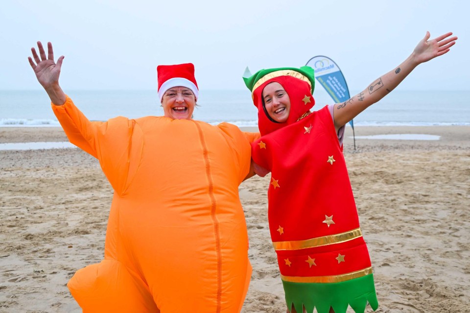 Two women in Christmas costumes on a beach.