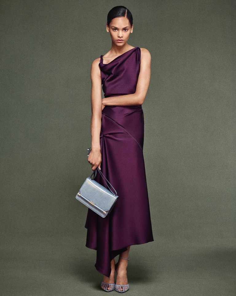 Model in purple asymmetrical midi dress and light blue handbag.