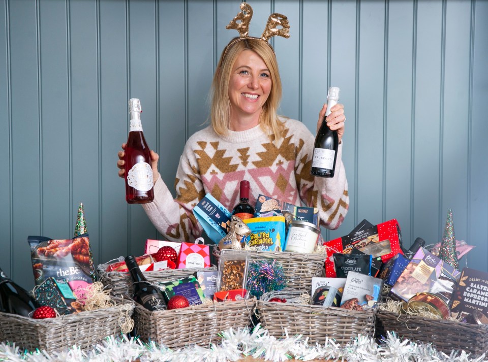 Woman with reindeer antlers holding three Christmas hampers filled with food and drink.