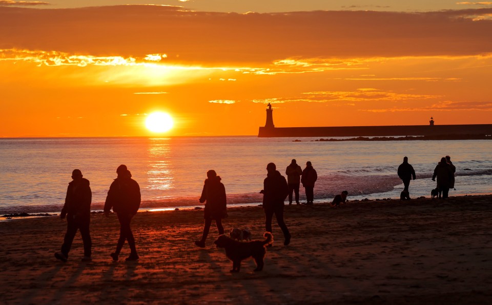 Silhouetted figures walking dogs on a beach at sunrise on Christmas Day.