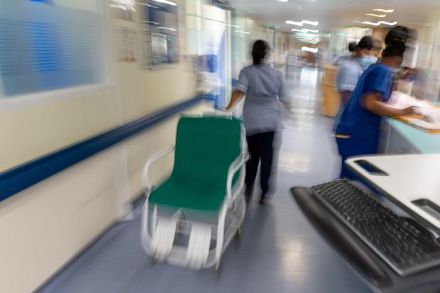 Blurred photo of hospital staff and a gurney in a hallway.