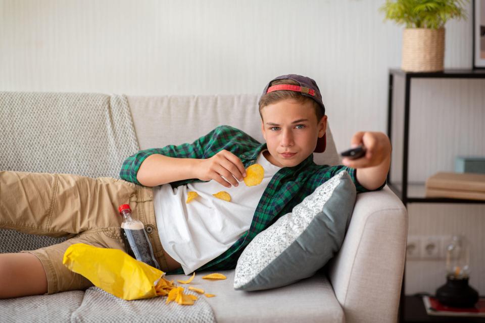 2CCRJ13 Teenager resting at home, watching TV and eating snacks