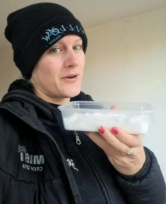 Woman demonstrating a damp home hack using rice in a takeaway container.