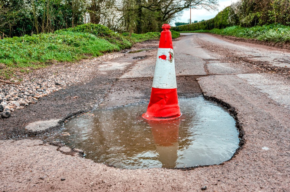 Traffic cone in a large pothole on a road.