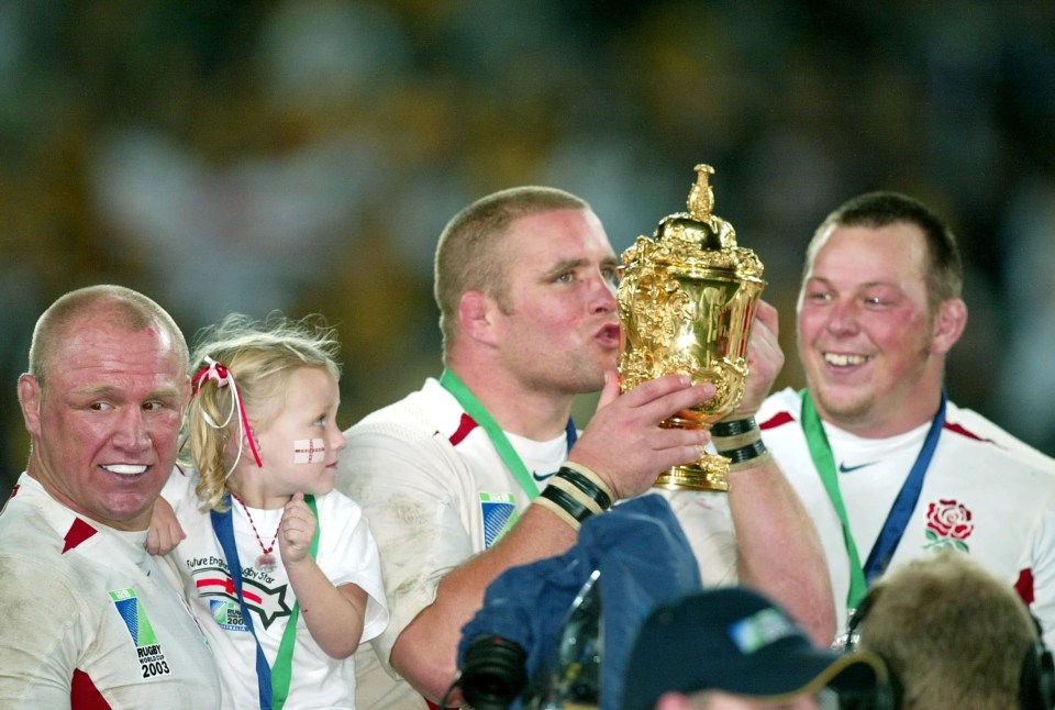 England's rugby players celebrate their World Cup victory with a young girl.