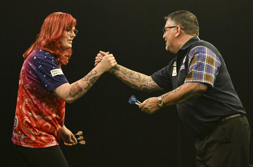 A photo of two men shaking hands, one is Noa-Lynn van Leuven wearing a blue shirt, and the other is Gary Anderson wearing a black shirt.