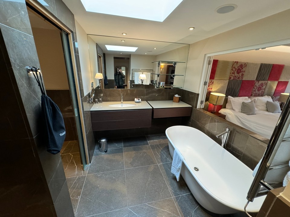 Luxurious hotel bathroom with freestanding bathtub and view into bedroom.