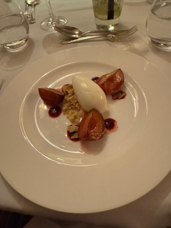 Plated dessert with roasted plums, ice cream, and almond crumble.