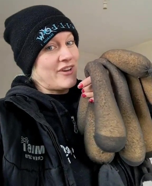 Woman demonstrating a damp home hack using filled takeaway containers.