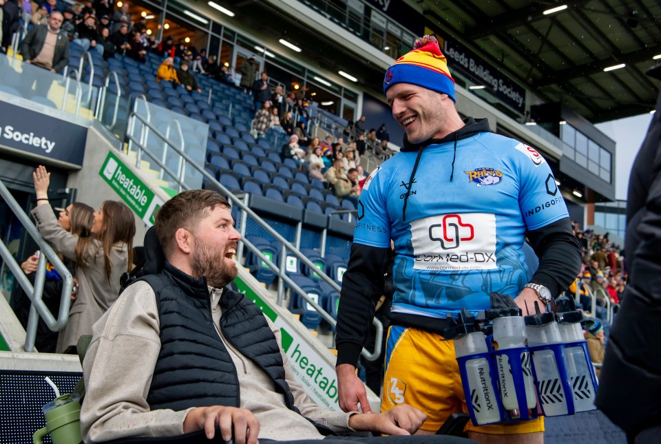 Tom Burgess at a rugby match, talking to a fan in a wheelchair.