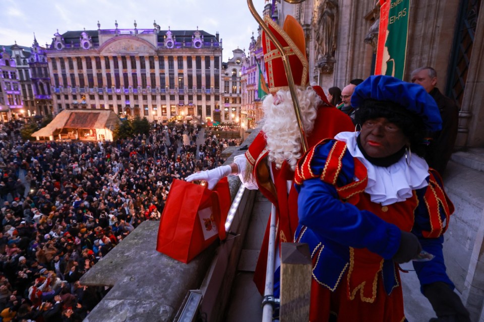 epa11749748 A person dressed as Zwarten Piet greets spectators in front of a man dressed as Saint Nicolas on a balcony at Grand Place square as he arrives in Brussels, Belgium, 30 November 2024. Saint Nicolas is taking place on 06 December with presents for the children. Saint Nicholas is usually accompanied by Zwarten Pieten, aka Black Petes giving carbon to naughty children. Black Petes are people dressed up and wearing blackface makeup have been the subject of protests the last couple of years. EPA/OLIVIER HOSLET