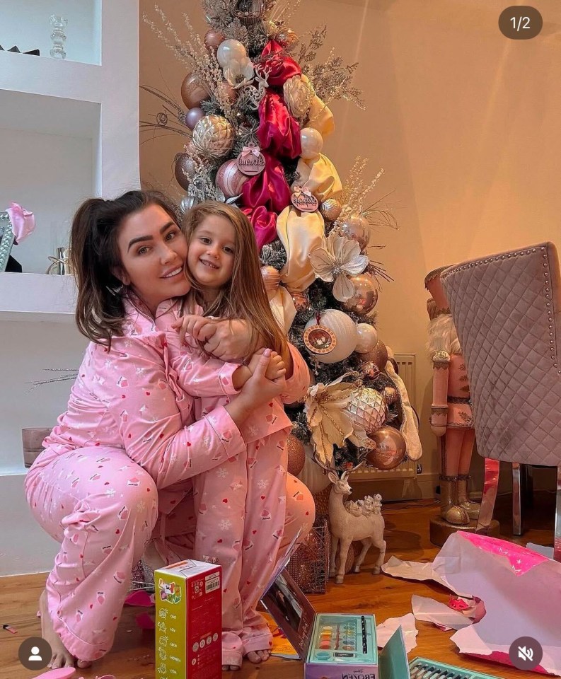 Woman and child in matching pink pajamas by a decorated Christmas tree.