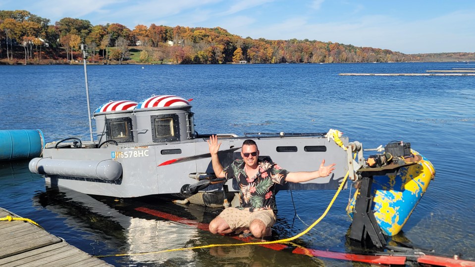 Man kneeling in the water next to a small boat.