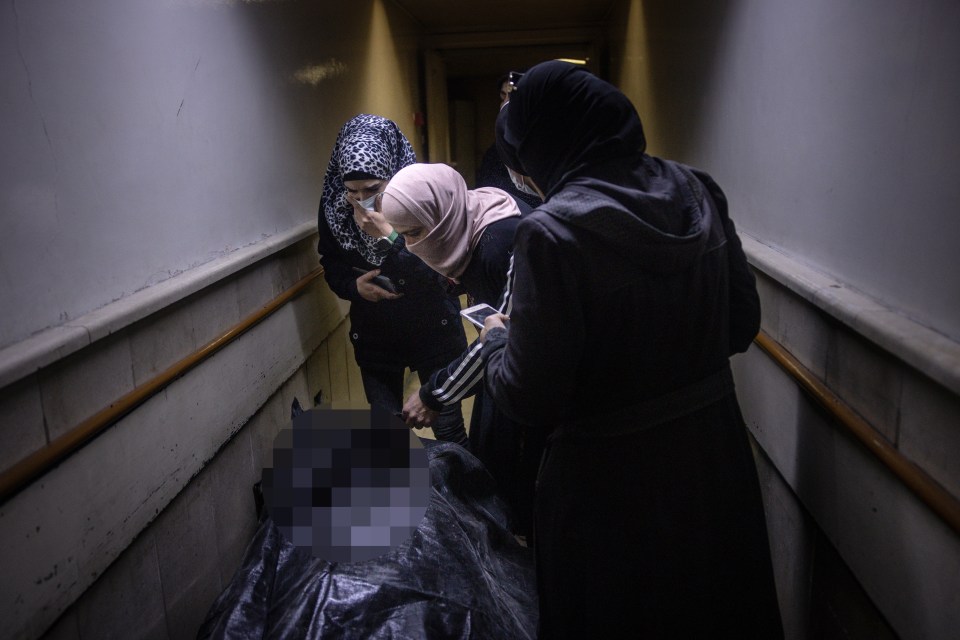 Women look at a body bag inside the morgue in Syria