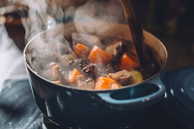 Steaming beef stew with vegetables in a blue cast iron pot.