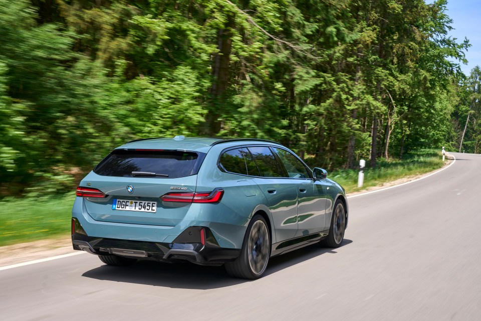 A light-blue BMW 3 Series Touring driving on a road through a forest.