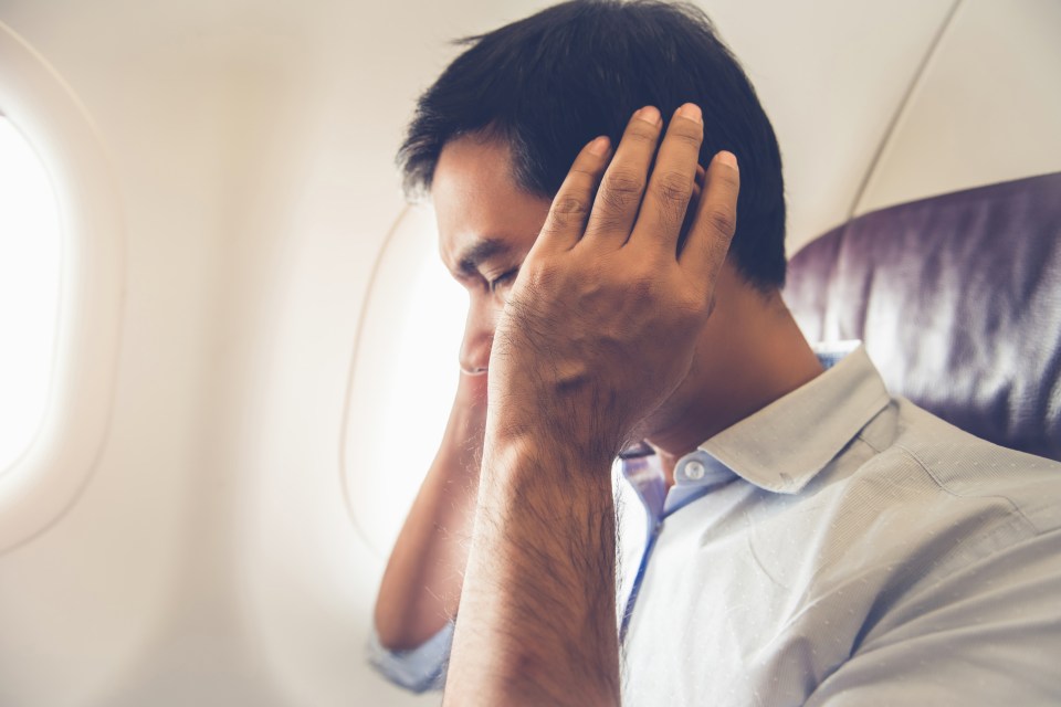 Man on airplane holding his ears, experiencing ear pain.