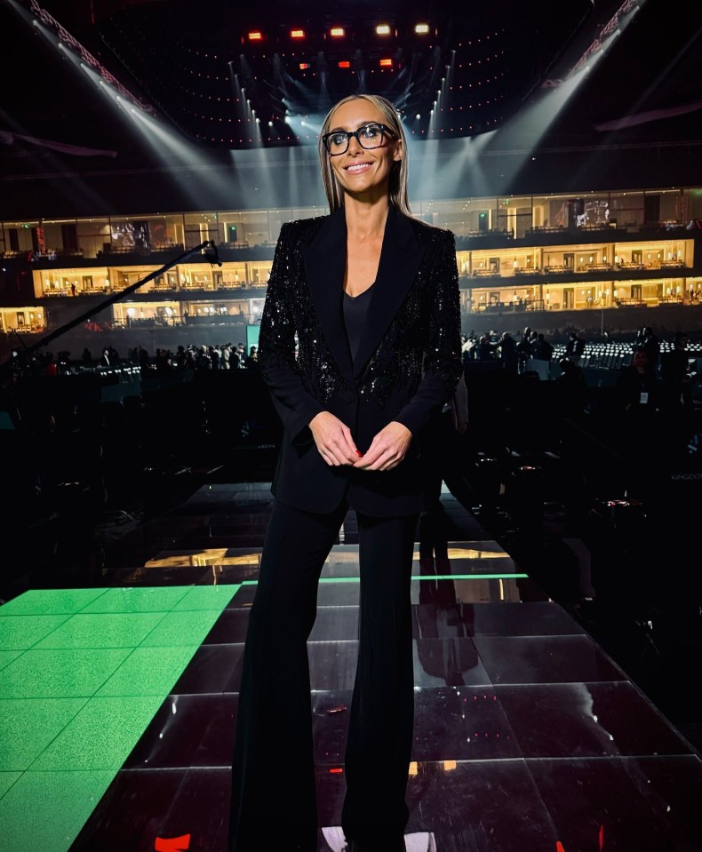 Woman in black sequined blazer and pants standing on stage.