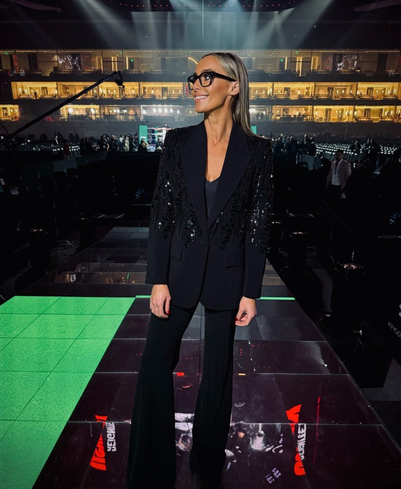 Woman in black sequined blazer and pants stands in large venue.