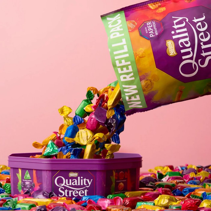 Quality Street candies pouring from a refill pack into a container.