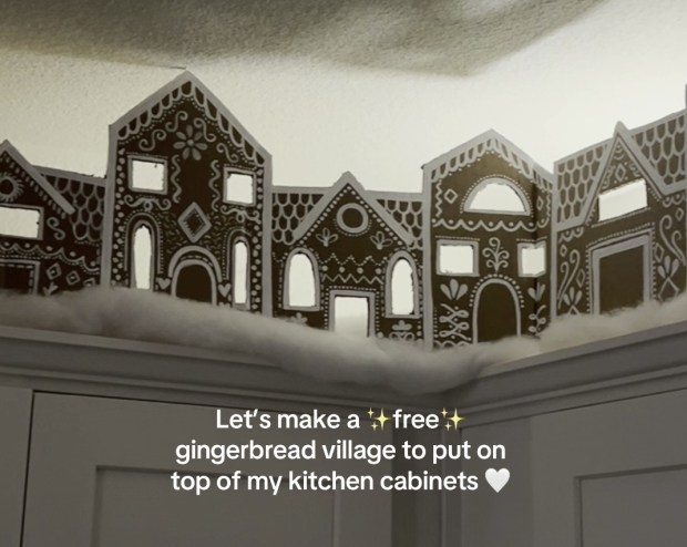 A hand holding a gingerbread village, a house, a tree and a reindeer, made out of old cardboard boxes, with a caption “Let’s make a free gingerbread village to put on top of my kitchen cabinets”.