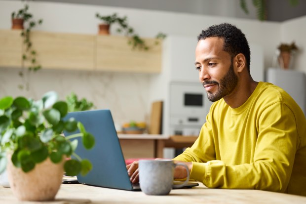 Confident young freelancer using laptop. Male is working from home. He is sitting at table.