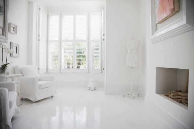 All-white living room with white shutters, fireplace, and armchair.