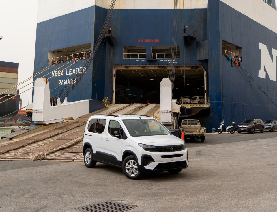 A white Peugeot e-Rifter electric vehicle being driven off a car carrier ship at the Port of Livorno.