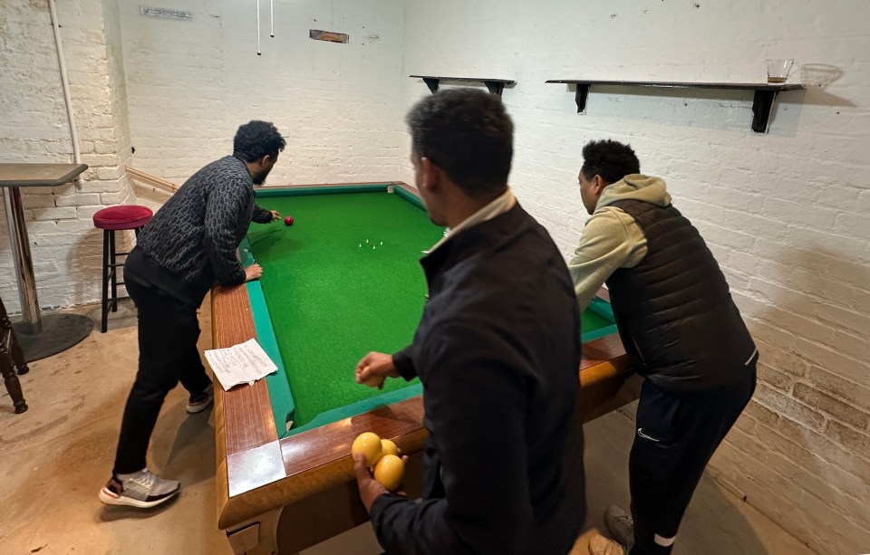 Three men playing Vilado, an Italian pool game, in a back room.