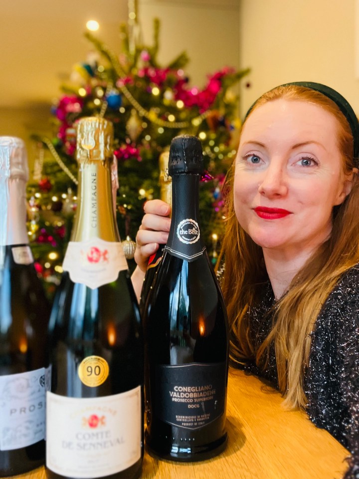 Woman holding bottles of champagne and prosecco in front of a Christmas tree.