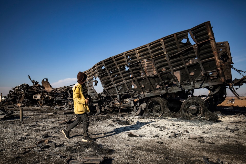 A boy walks past a destroyed military vehicle in Qamishli the day after Israeli airstrikes