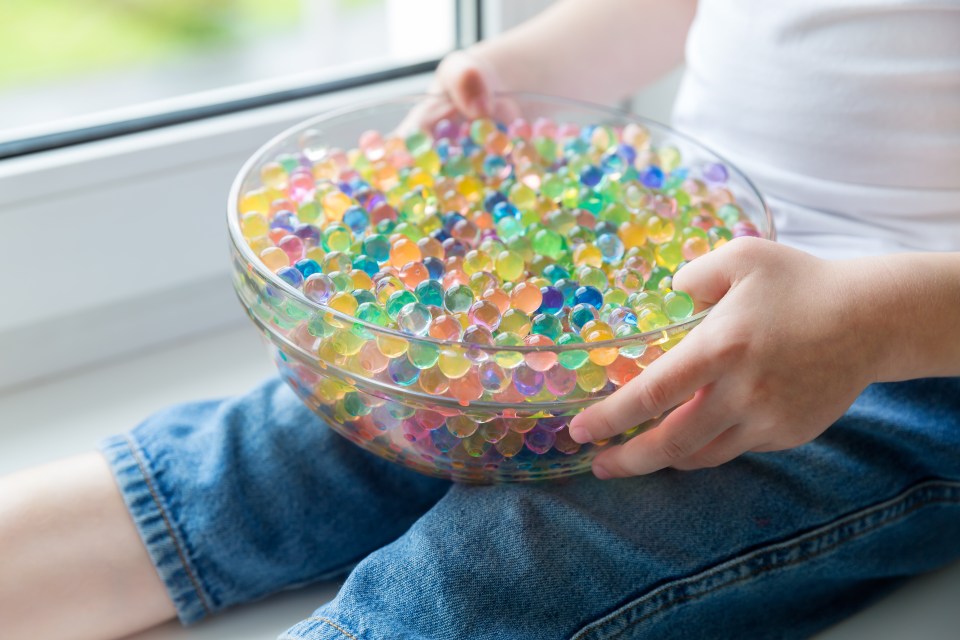 Child playing with colorful hydrogel beads in a glass bowl.