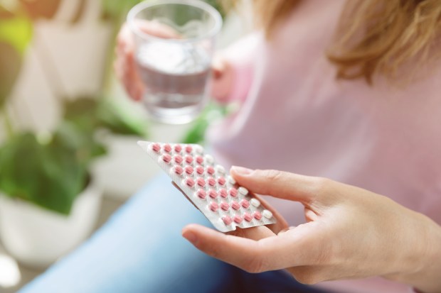 Woman holding birth control pills and a glass of water.