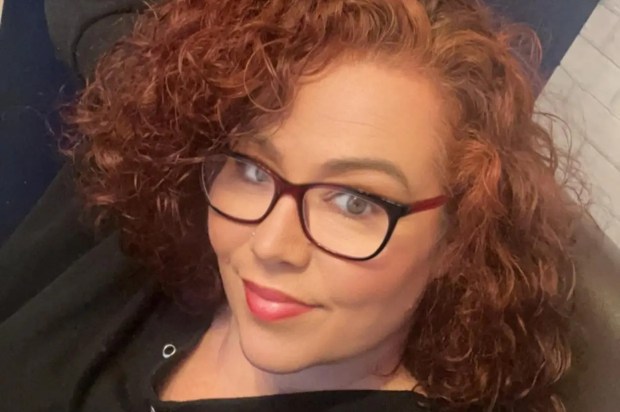 Headshot of a woman with curly auburn hair wearing glasses.