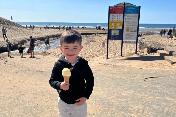 Toddler holding ice cream cone on beach.