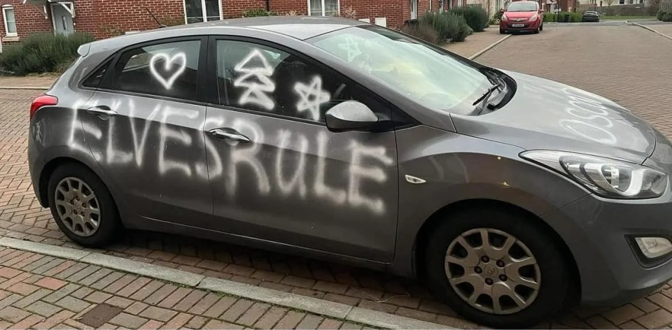 A gray car vandalized with graffiti that says "Elves Rule".