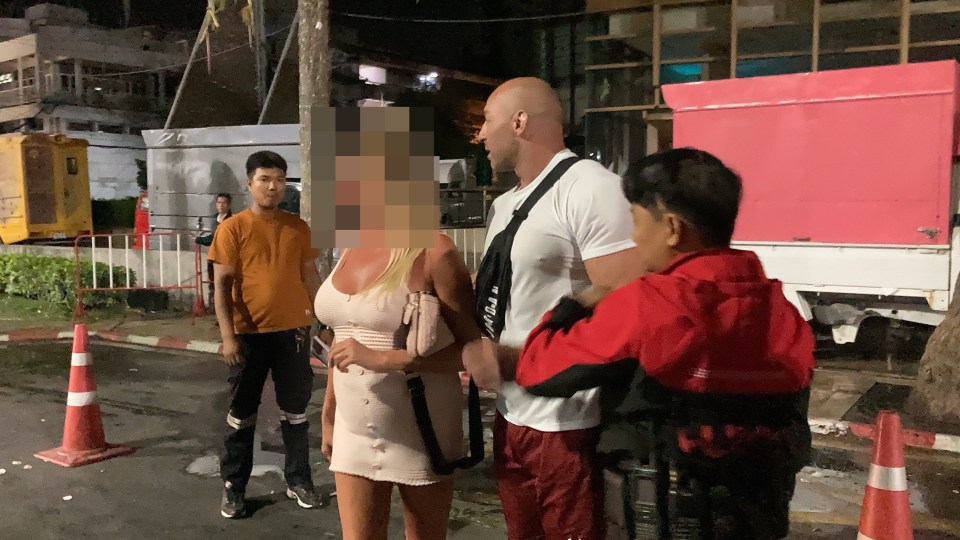 A blonde woman in a white dress is being detained by police in Thailand.