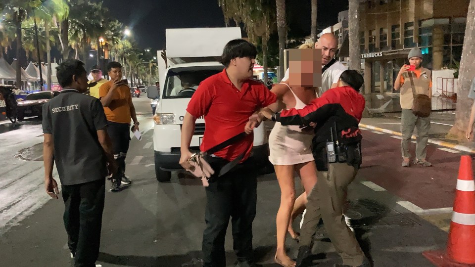 A woman in a white dress is being detained by police officers on a street at night.