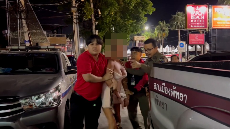 A handcuffed woman in a white dress is being escorted by police officers.