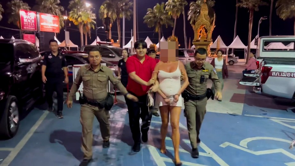 A handcuffed woman in a white dress is escorted by police officers.