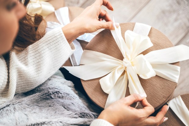 Woman tying a pastel ribbon on a gift box.