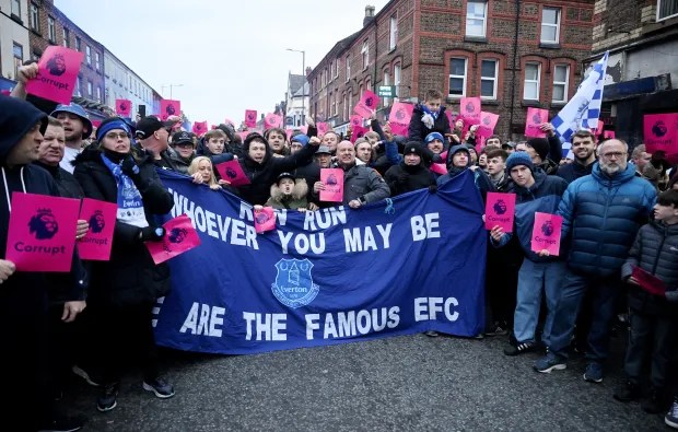 Everton fans protesting, holding signs that say "Corrupt" and a banner reading, "Whoever you may be are the famous EFC".