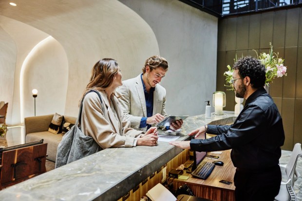 Medium shot of couple using digital tablet to check in at front desk in hotel lobby during business trip