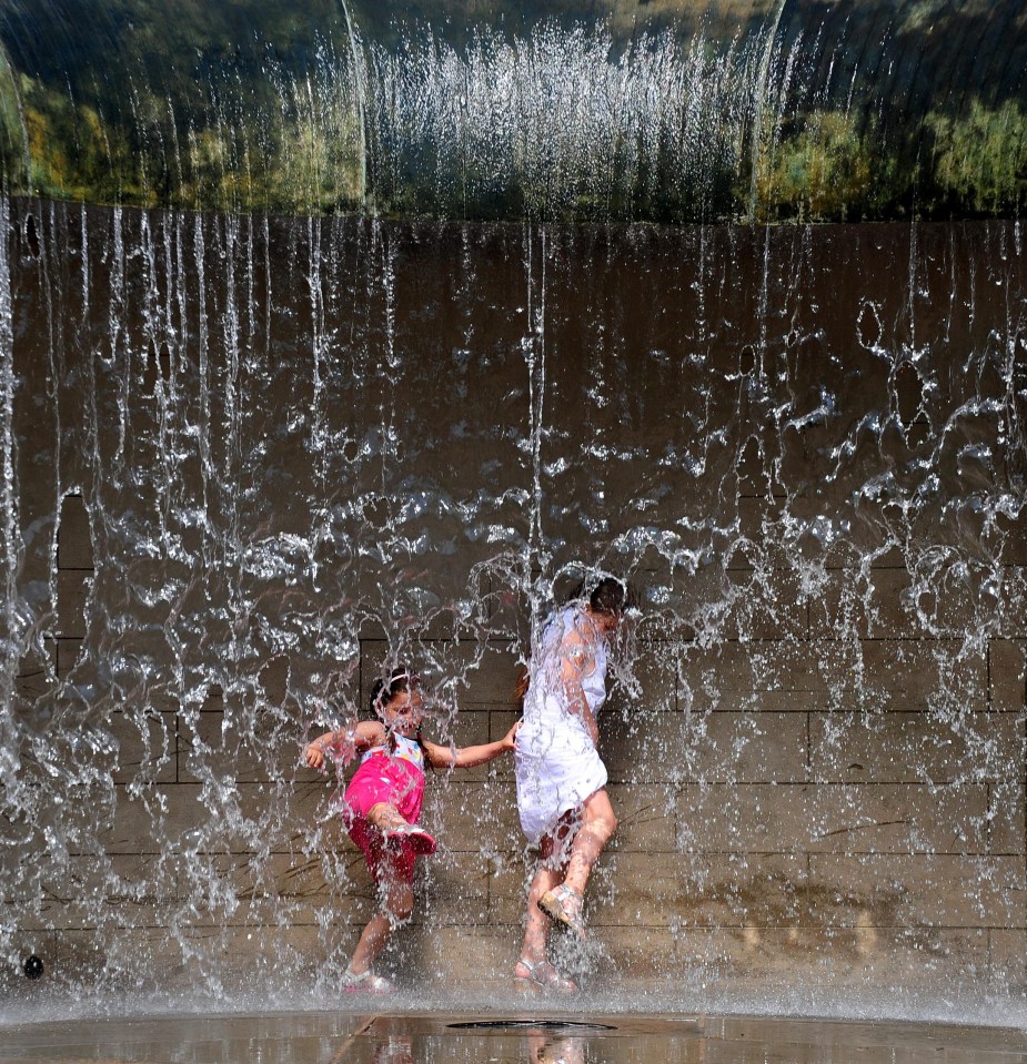 Two young girls playing in a city fountain.