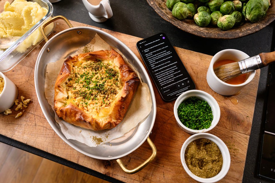 Baked potato and cheese dish with recipe on phone screen.