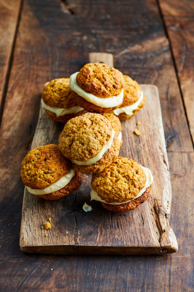 Several cream-filled cookies stacked on a wooden board.