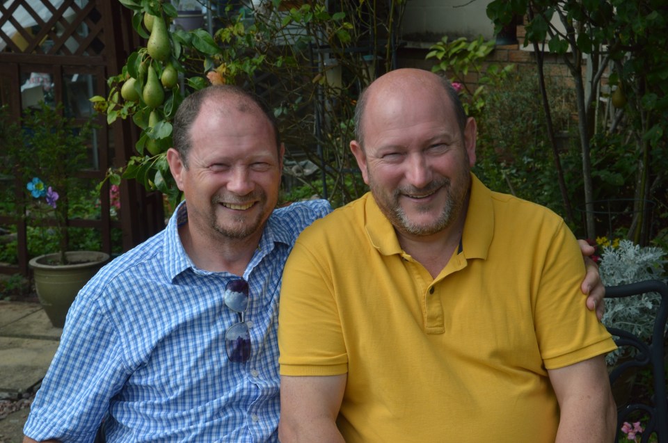 Two men smiling and sitting together outdoors.