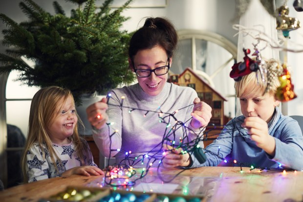 A woman and two children are decorating the Christmas tree with lights.