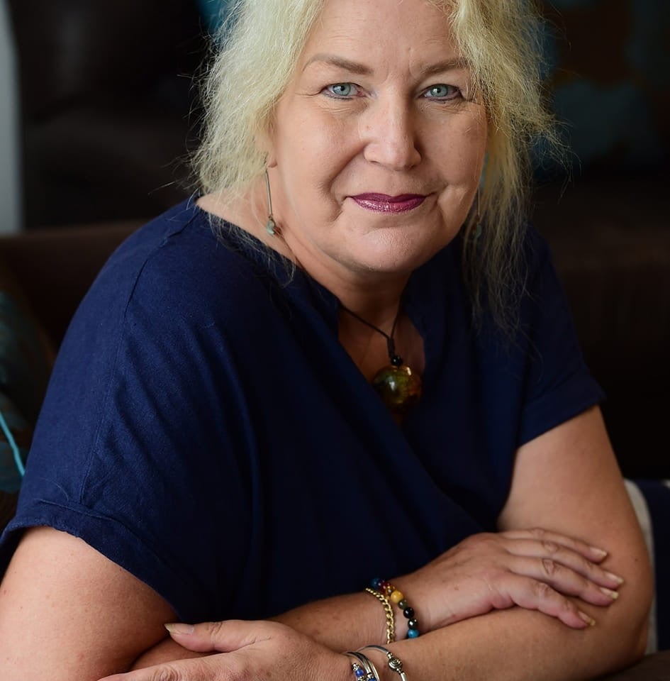 Portrait of a woman with blonde hair, wearing a dark blue shirt and bracelets.